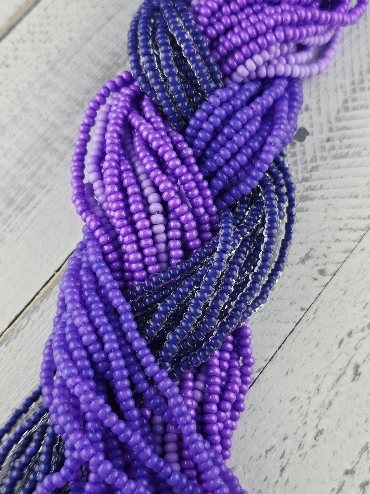 A close-up view of a collection of colorful beads, predominantly purple and blue, arranged in a twisted or braided pattern on a wooden surface.