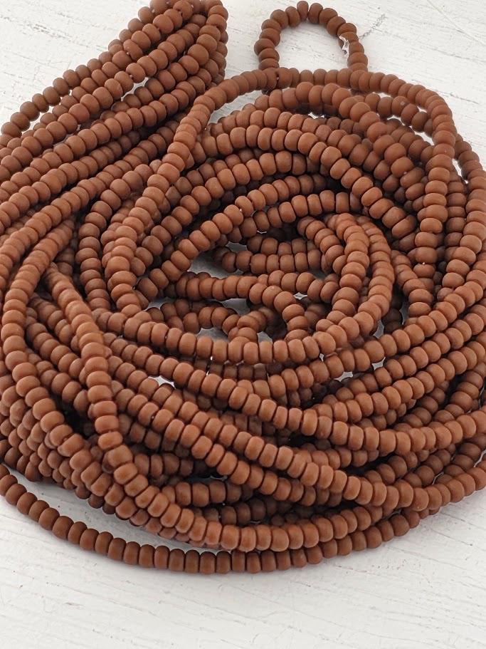 A large pile of brown beads, possibly made of glass or plastic, arranged in a spiral pattern on a white surface.