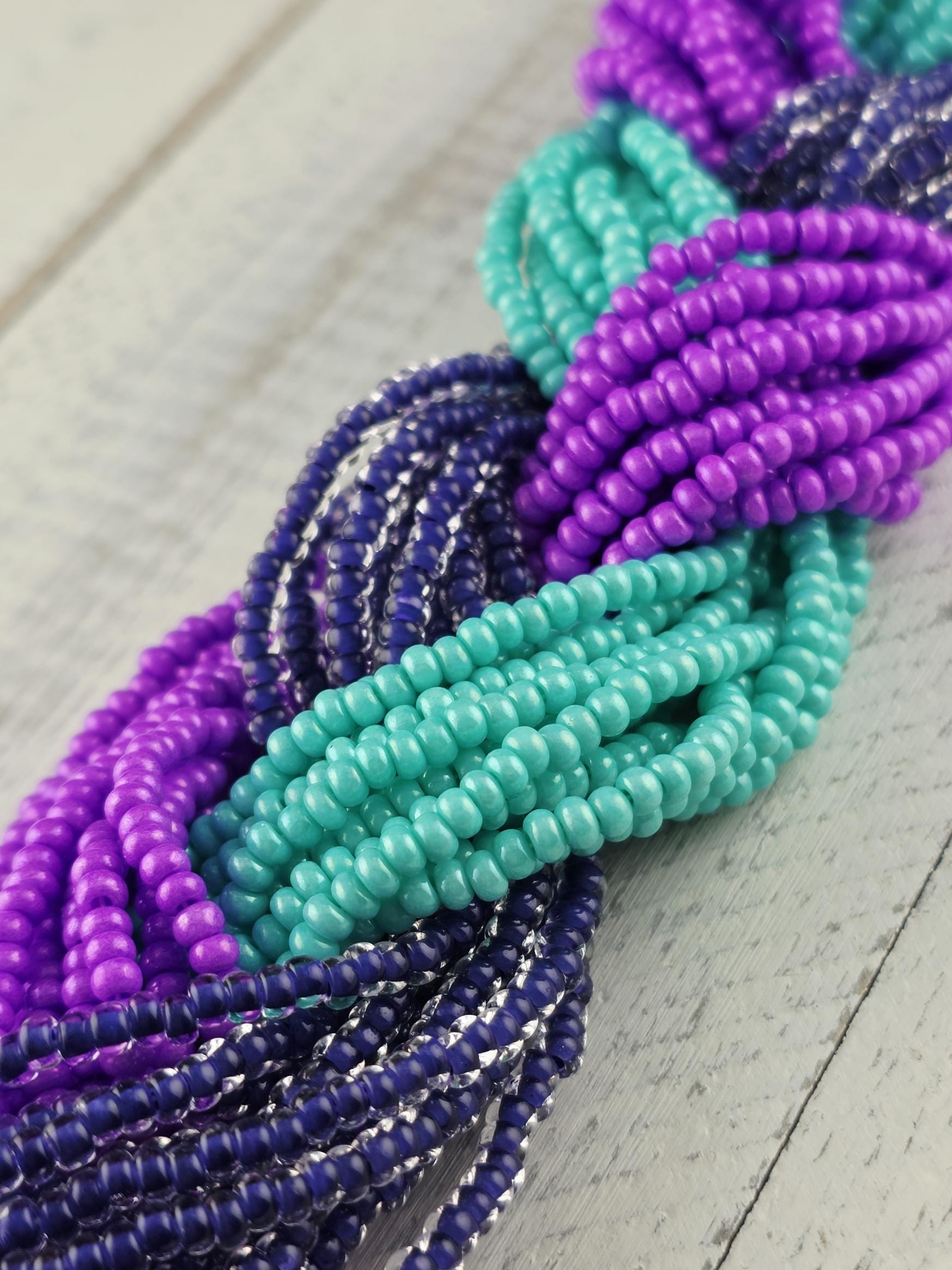 A close-up view of a collection of colorful beads, including purple, blue, and green beads, arranged in a tangled and intricate pattern.