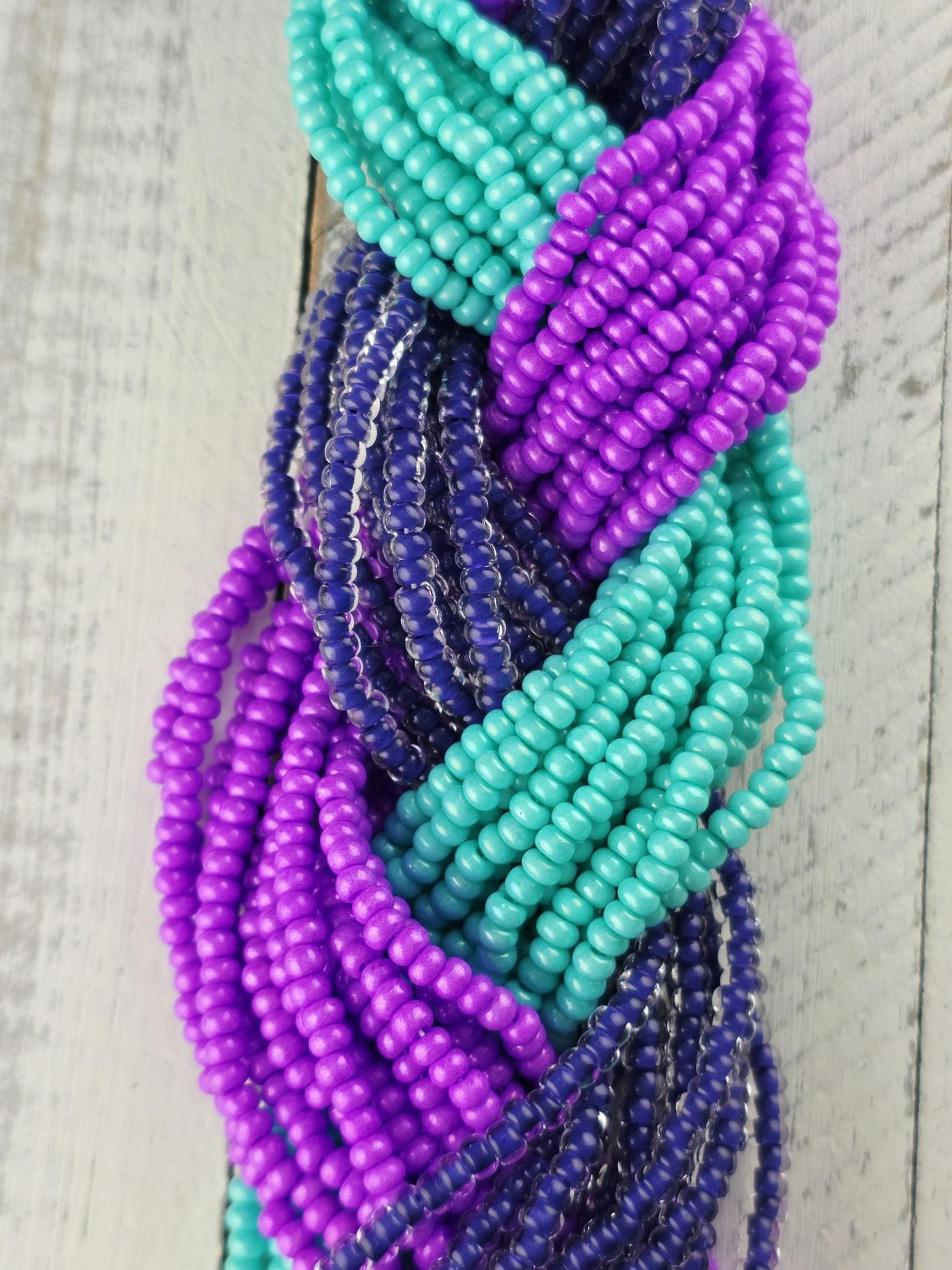 A close-up view of a collection of colorful beads, including purple, blue, and green beads, arranged in a braided pattern on a wooden surface.