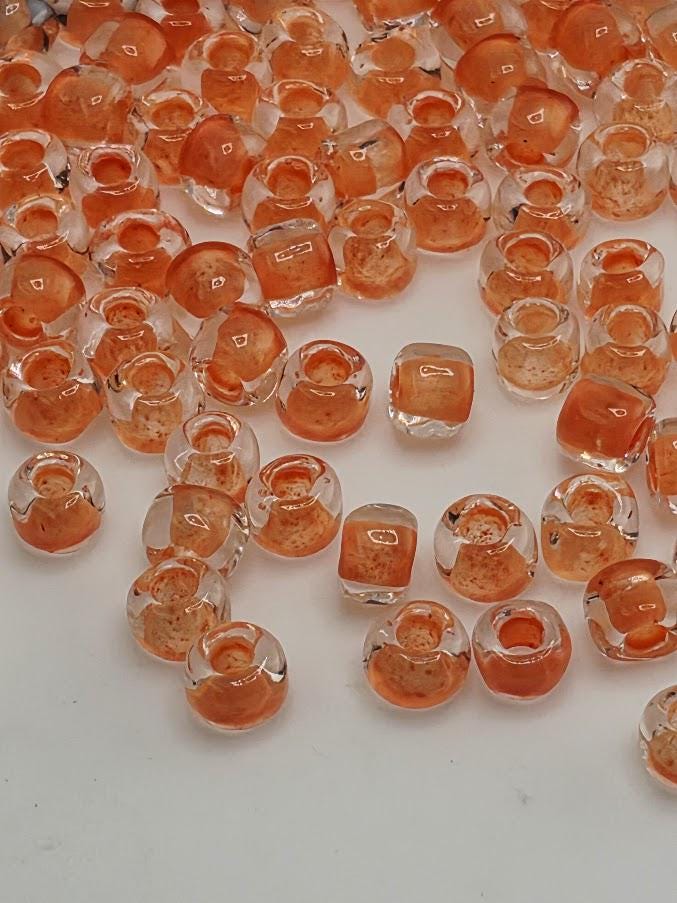a collection of small, clear glass beads in various shades of orange, scattered across a white surface.