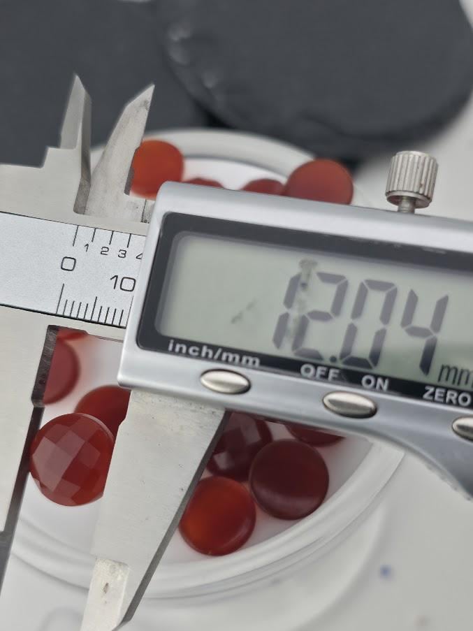 A digital caliper is being used to measure the diameter of a red object, which appears to be a small red ball or bead.