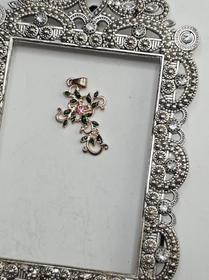 a decorative pendant with a floral design and a pink gemstone, placed within an ornate, silver-colored frame.