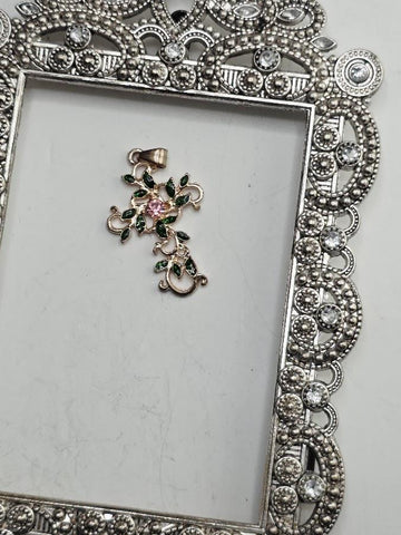 a decorative pendant with a floral design and a pink gemstone, placed within an ornate, silver-colored frame.