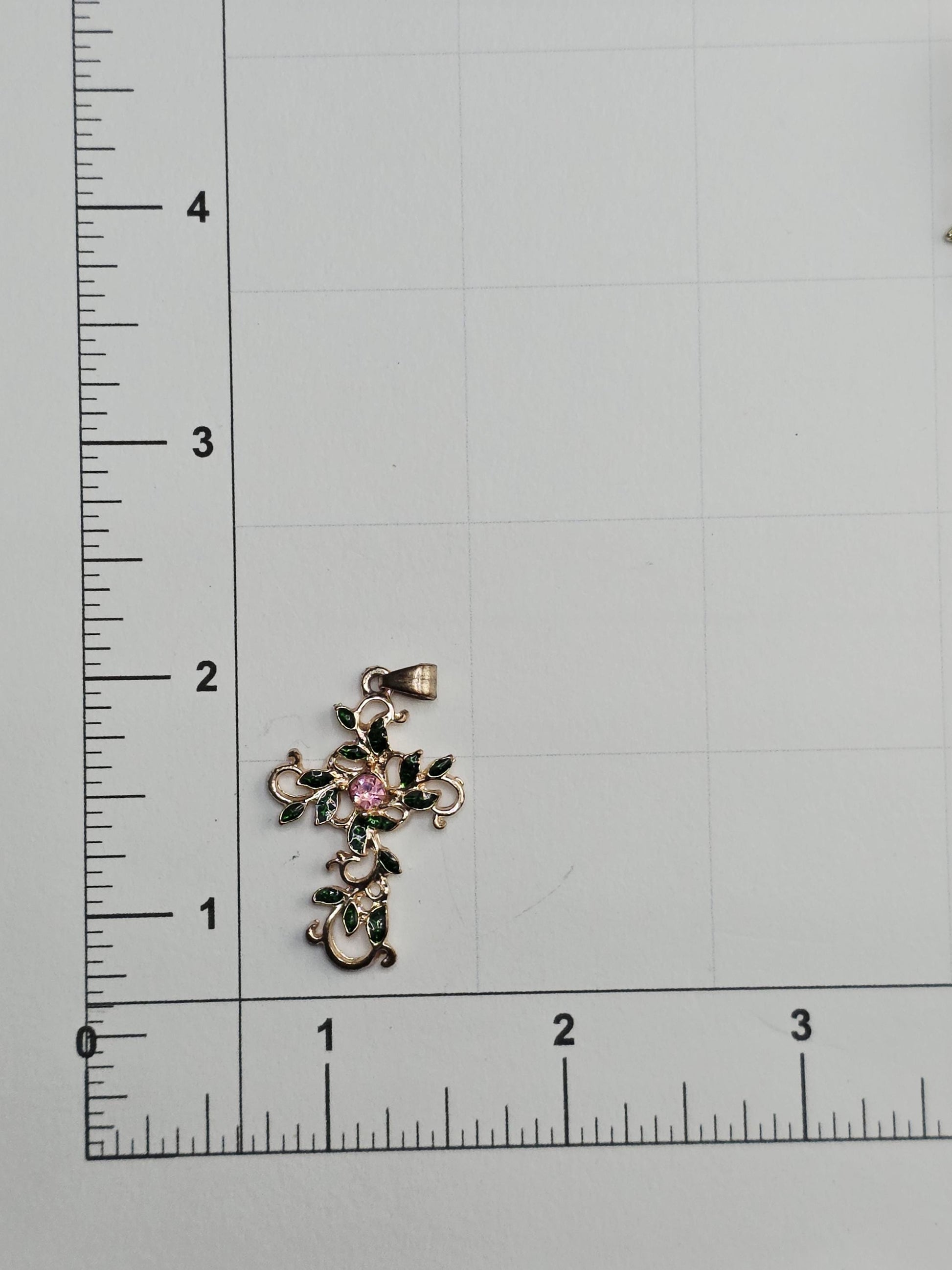 a pendant with a floral design placed on a ruler for size comparison.