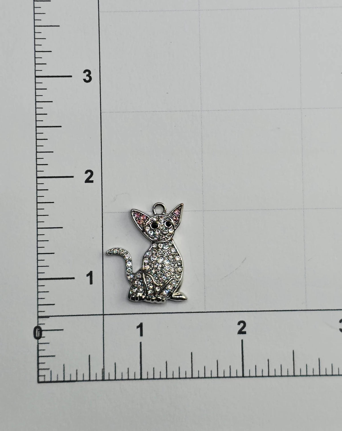 a small cat charm with rhinestones on it, placed on a ruler for size comparison.