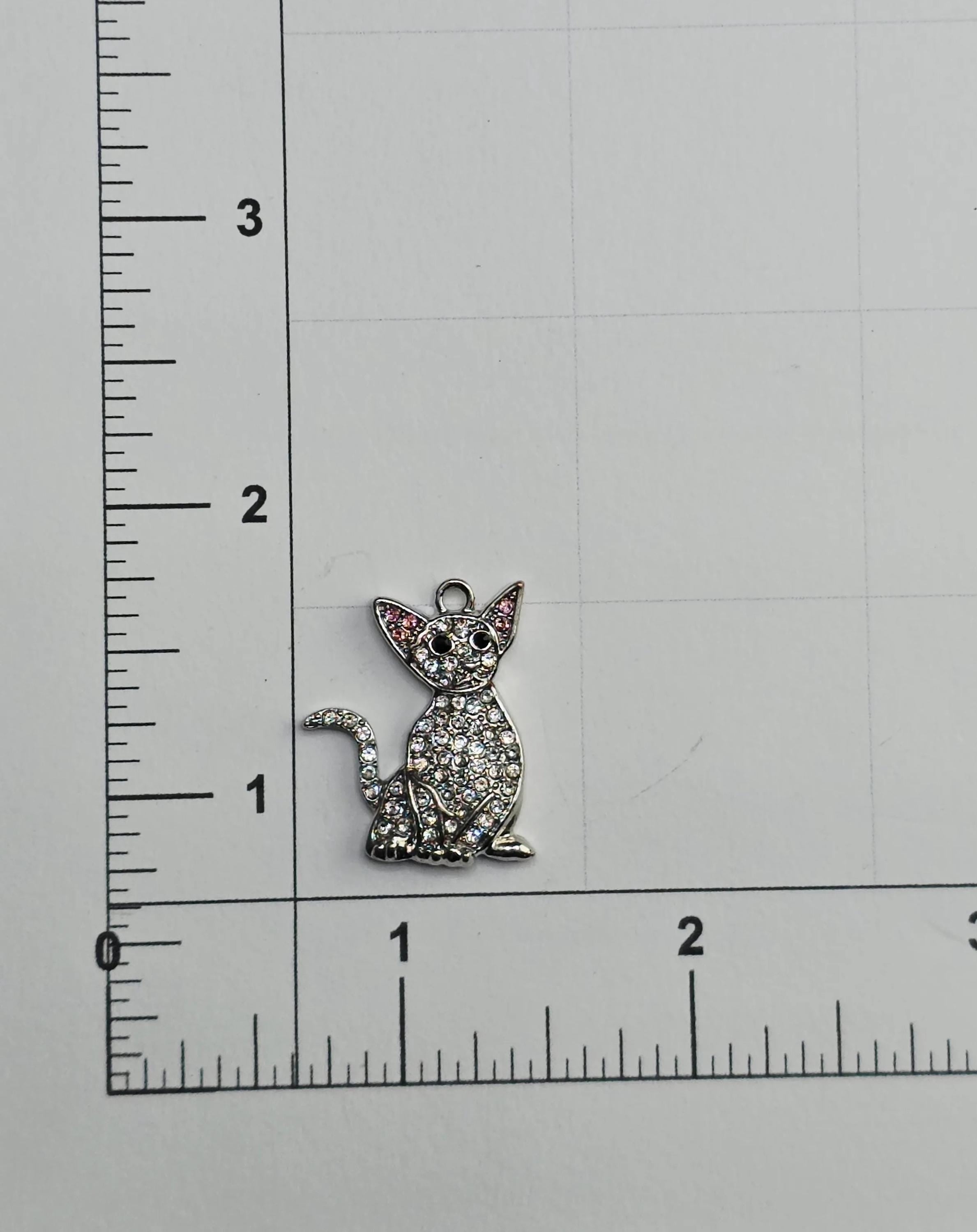 a small cat charm with rhinestones on it, placed on a ruler for size comparison.