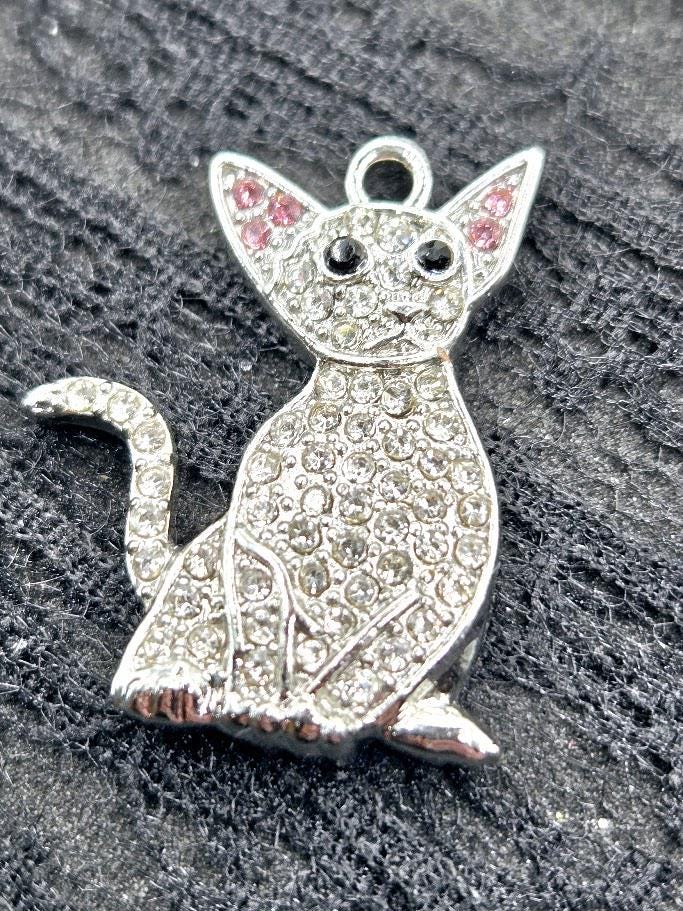 A silver-colored charm in the shape of a cat, adorned with sparkling rhinestones or crystals.