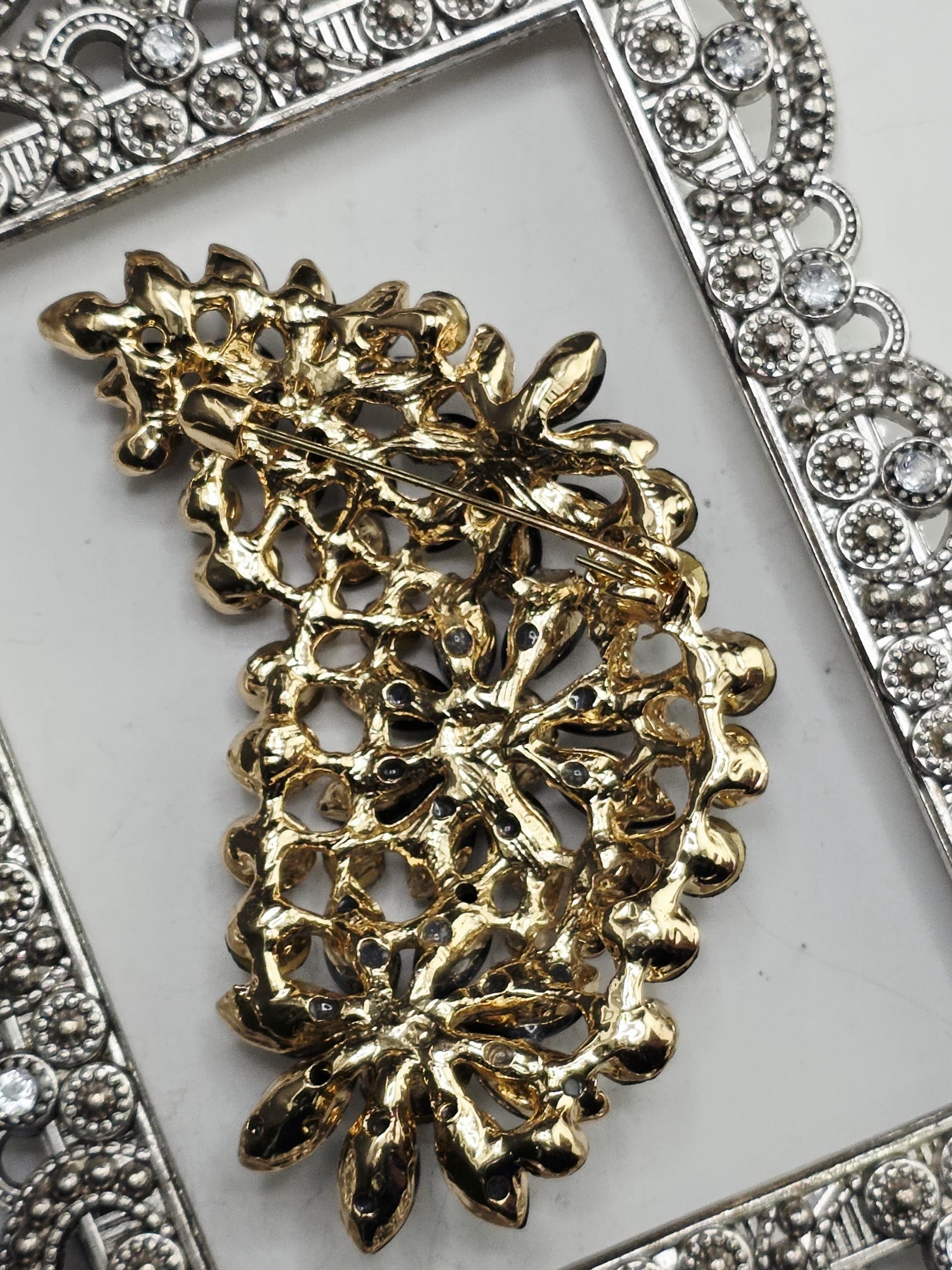 a decorative piece of jewelry, possibly a brooch or a necklace, with intricate floral designs and a metallic frame.