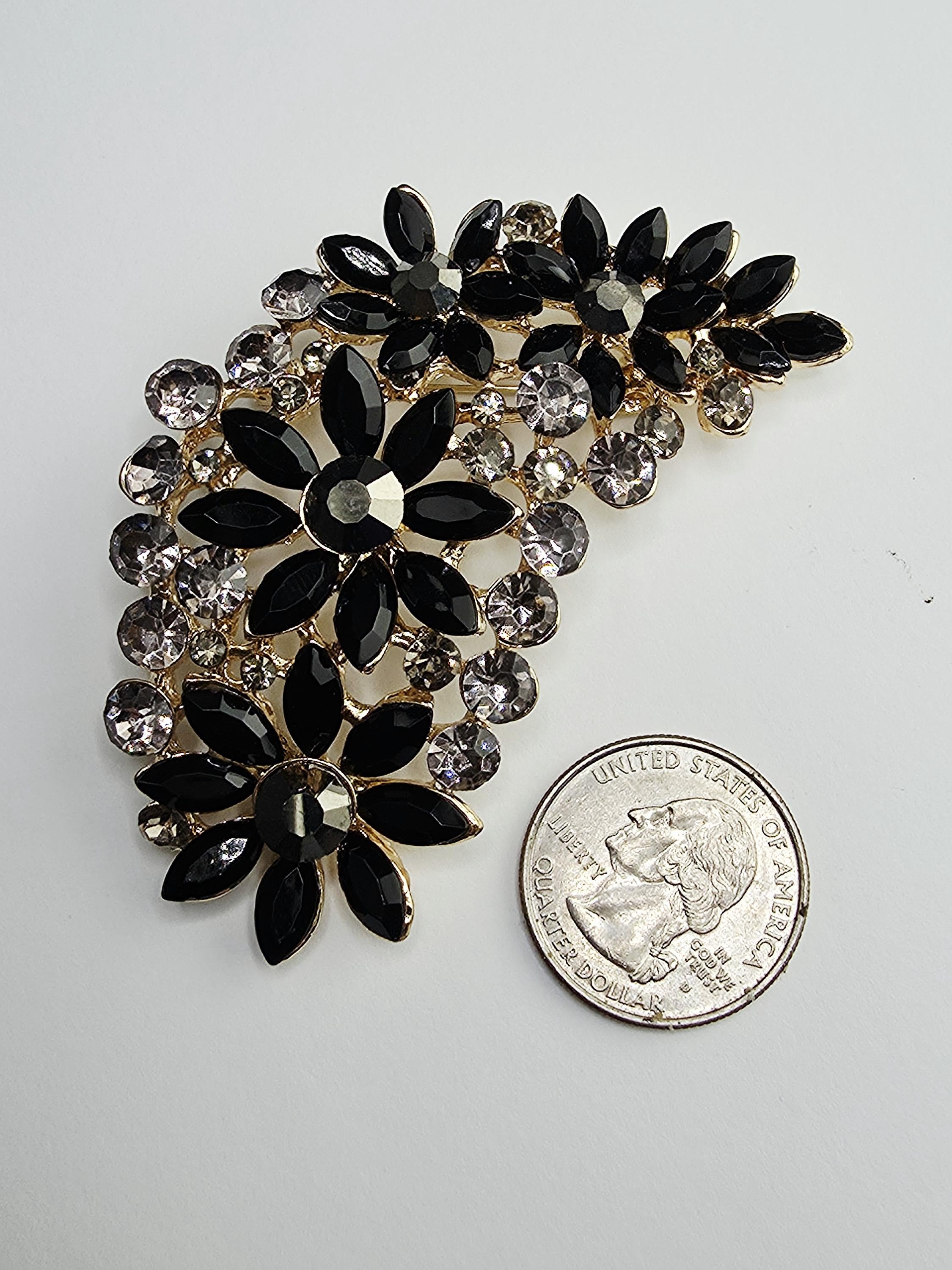 a decorative piece of jewelry, which appears to be a brooch or pendant, adorned with black and silver gemstones. The piece is placed next to a United States quarter, indicating its value.