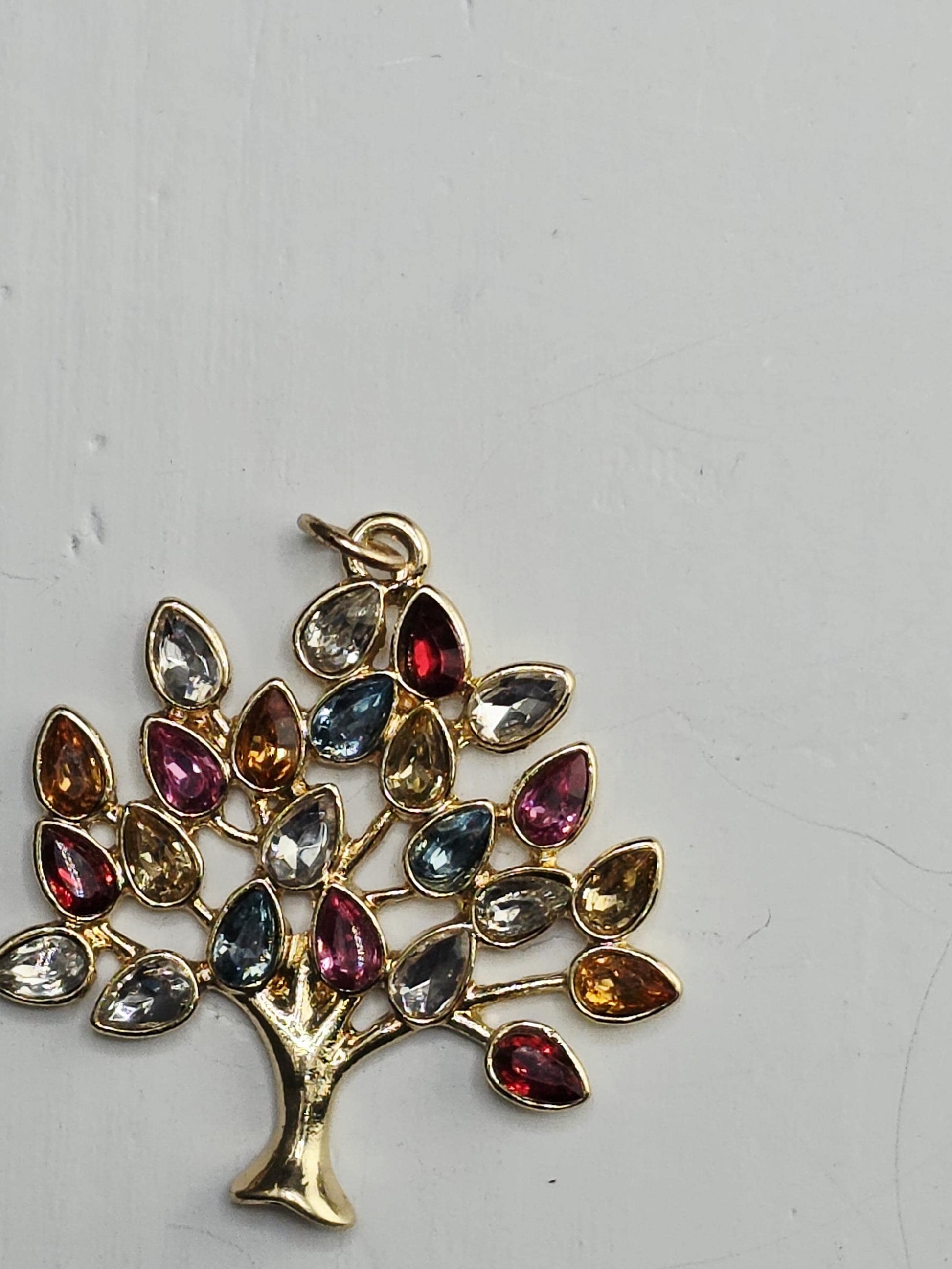 A decorative tree-shaped pendant made of colorful gemstones, including various shades of red, orange, yellow, green, blue, and purple.