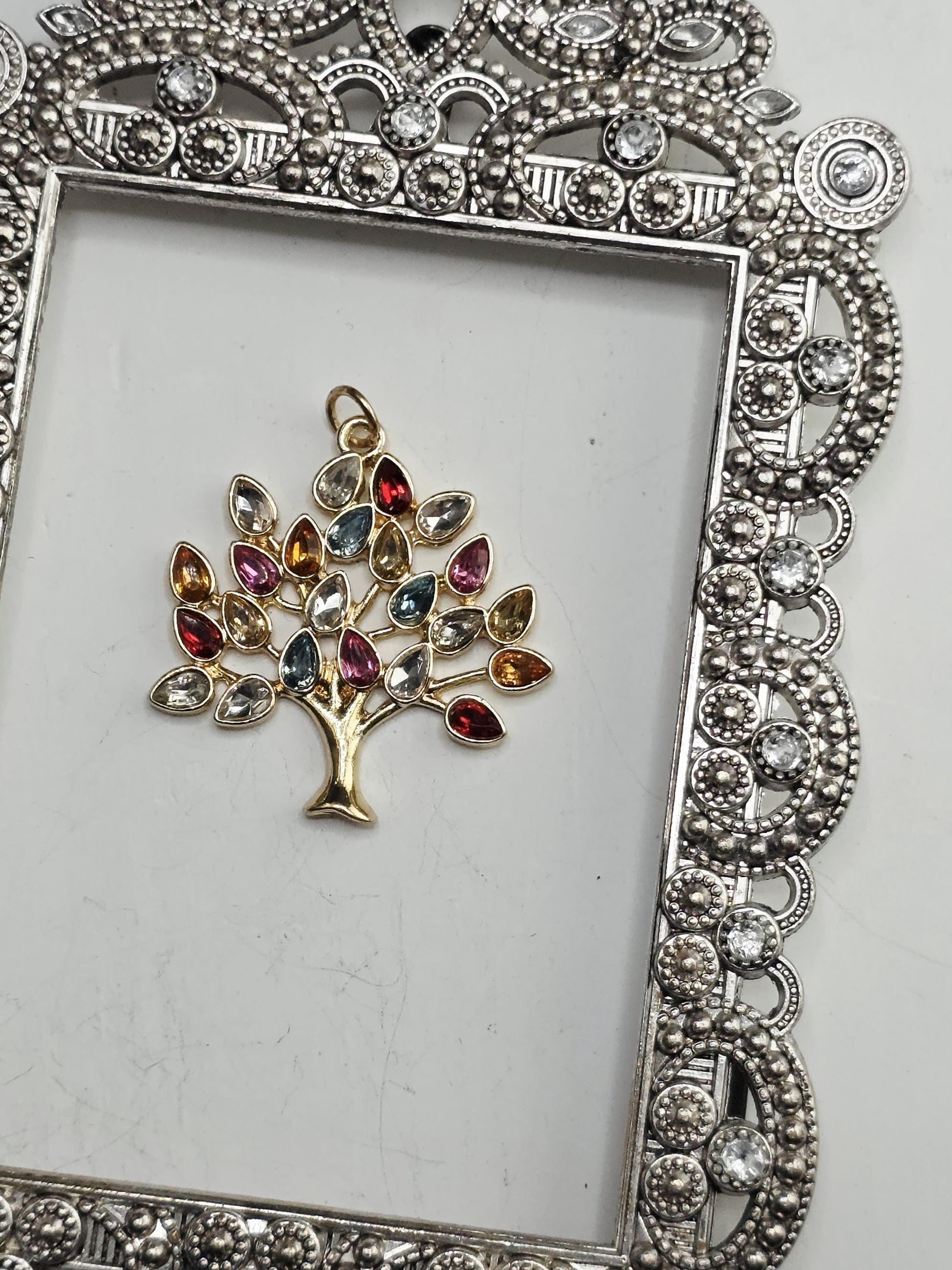 A decorative silver frame with a tree-shaped pendant made of colorful gemstones.