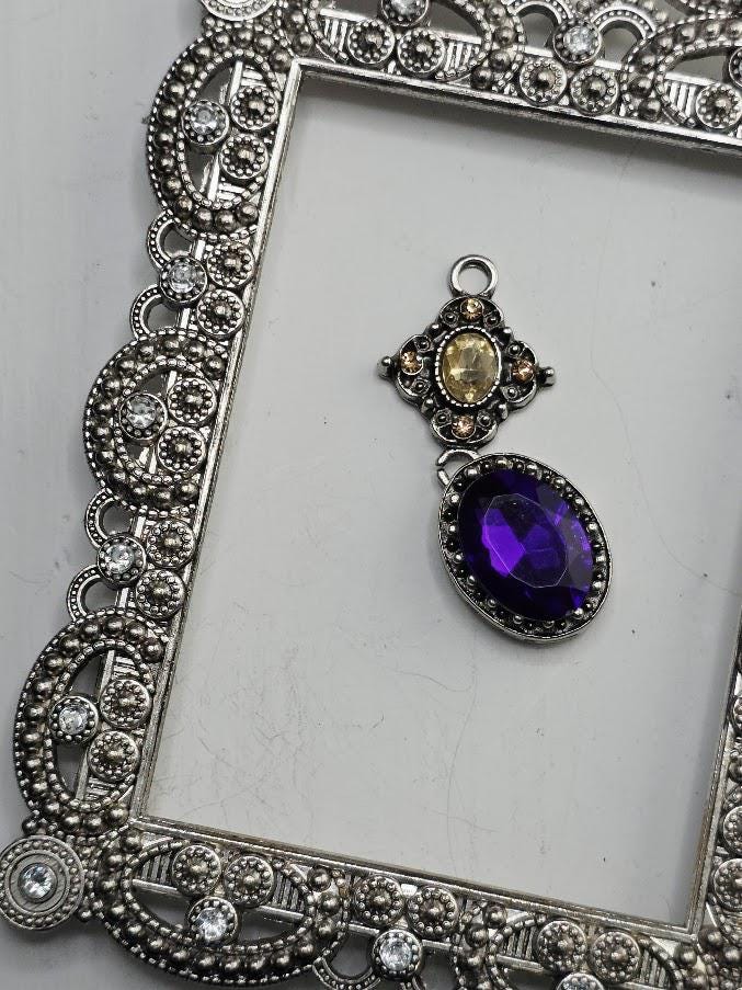 a silver ornate frame with a large purple gemstone hanging from it.