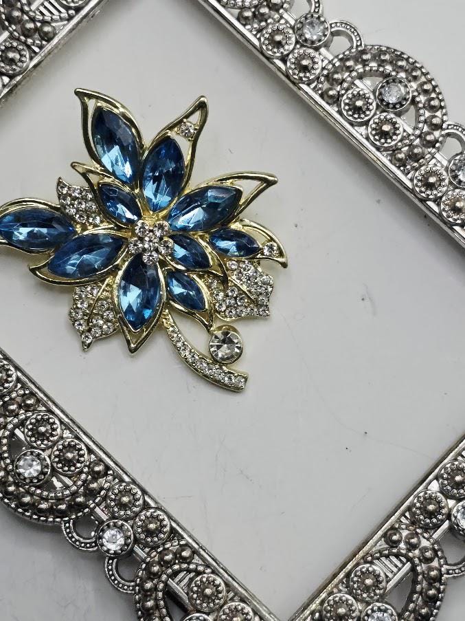 A decorative piece of jewelry featuring a blue gemstone surrounded by a metallic frame with intricate designs.