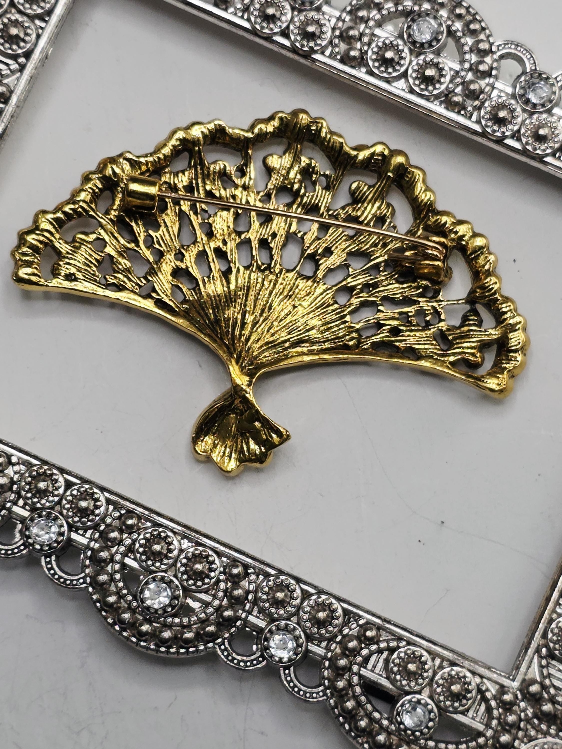 a decorative gold brooch with a fan-like design, placed on a white surface.