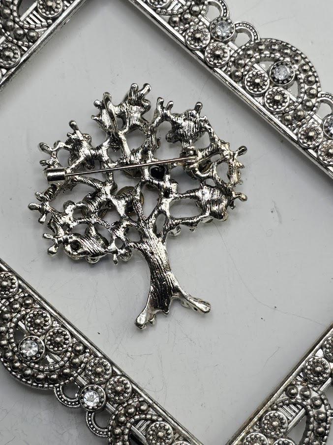 A decorative tree brooch with a variety of colorful gemstones, including red, blue, green, yellow, and pink, is displayed on a white surface.