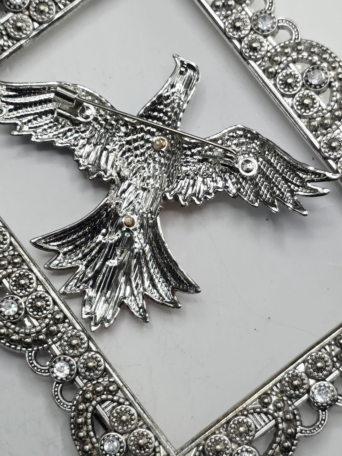 a close-up view of a decorative silver eagle brooch with intricate details and a metallic frame.