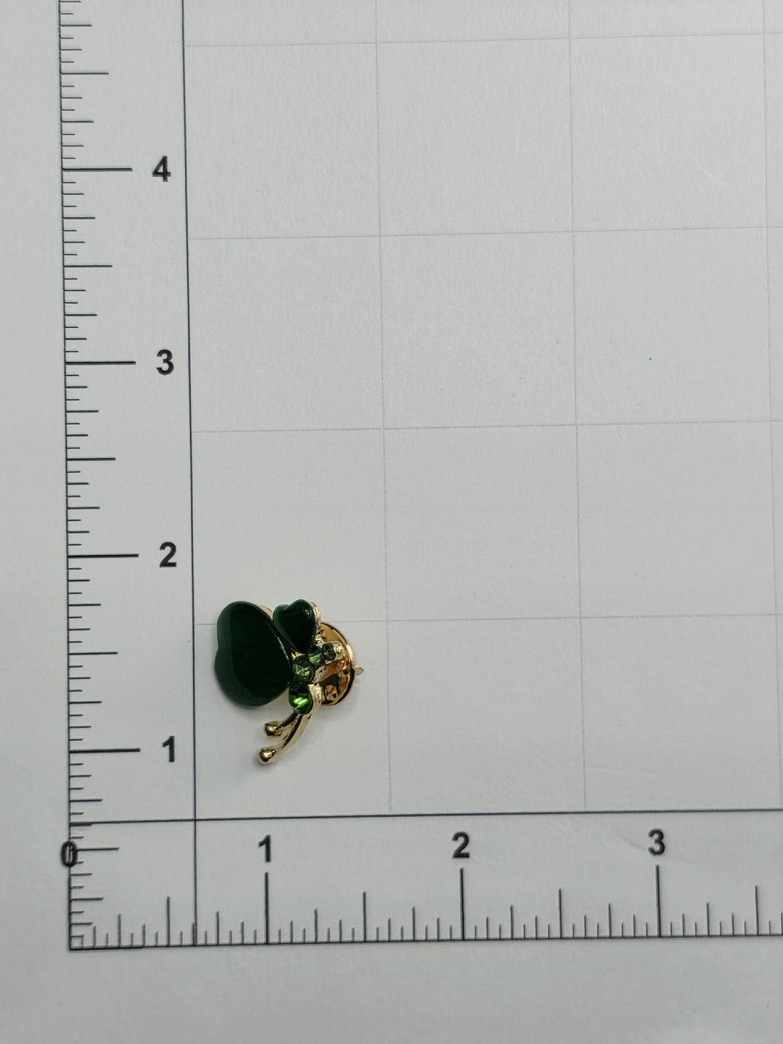a small, gold-colored pin placed on a white surface next to a ruler for size comparison.