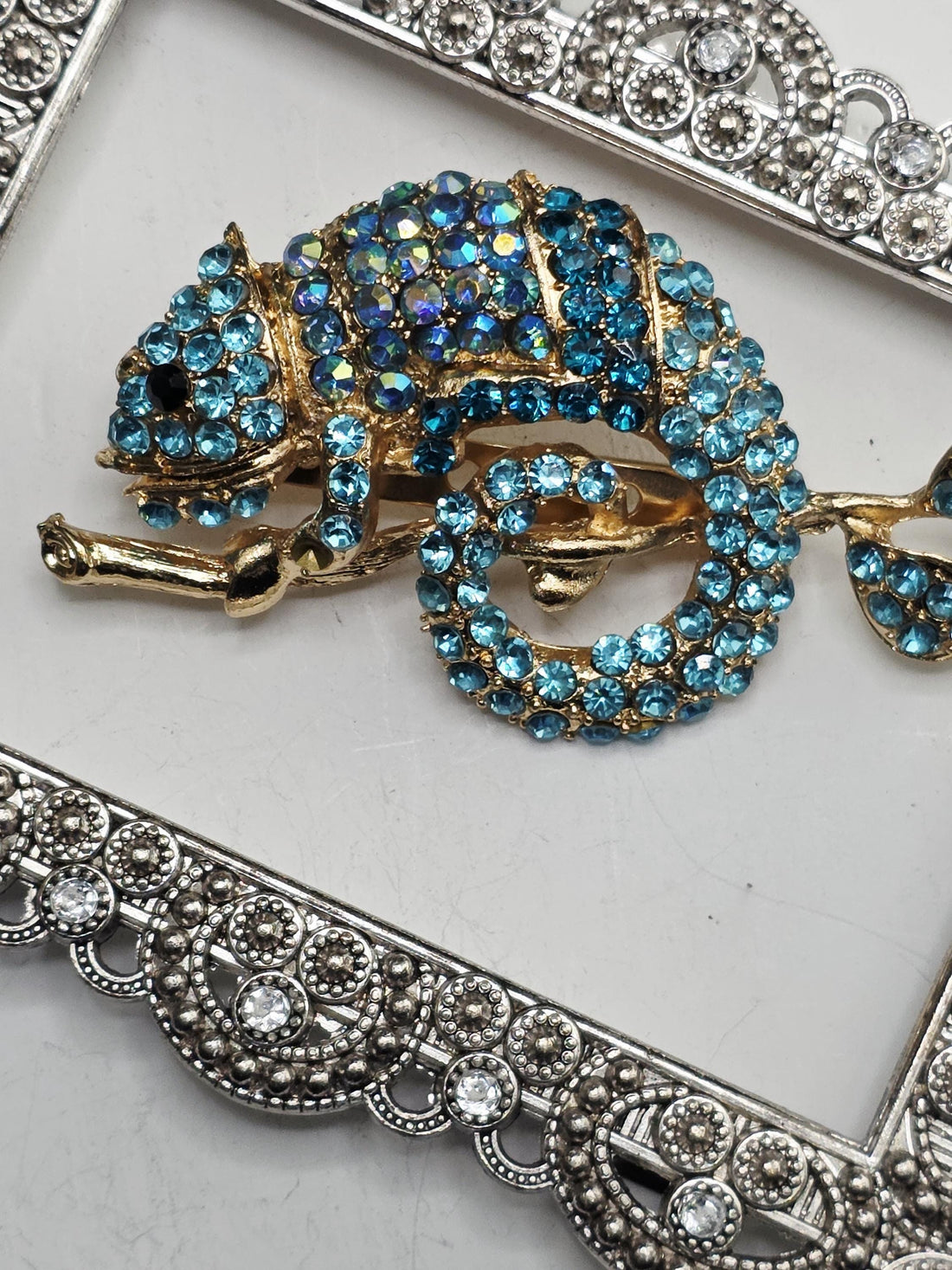 A decorative pendant with a blue and gold design, featuring a large blue gemstone surrounded by smaller blue gemstones. The pendant is set within an ornate, silver-colored frame.