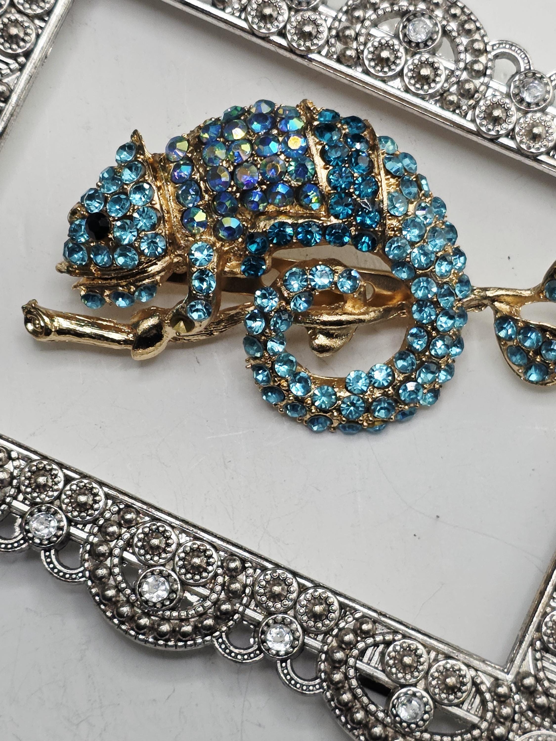 A decorative pendant with a blue and gold design, featuring a large blue gemstone surrounded by smaller blue gemstones. The pendant is set within an ornate, silver-colored frame.
