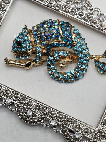 A decorative pendant with a blue and gold design, featuring a large blue gemstone surrounded by smaller blue gemstones. The pendant is set within an ornate, silver-colored frame.