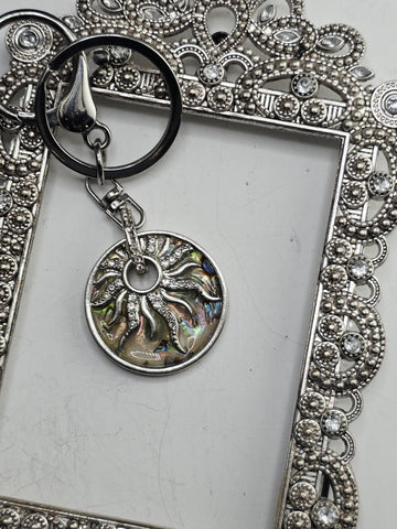 a silver-colored frame with a decorative border, and a round pendant with an intricate design hanging from the frame.