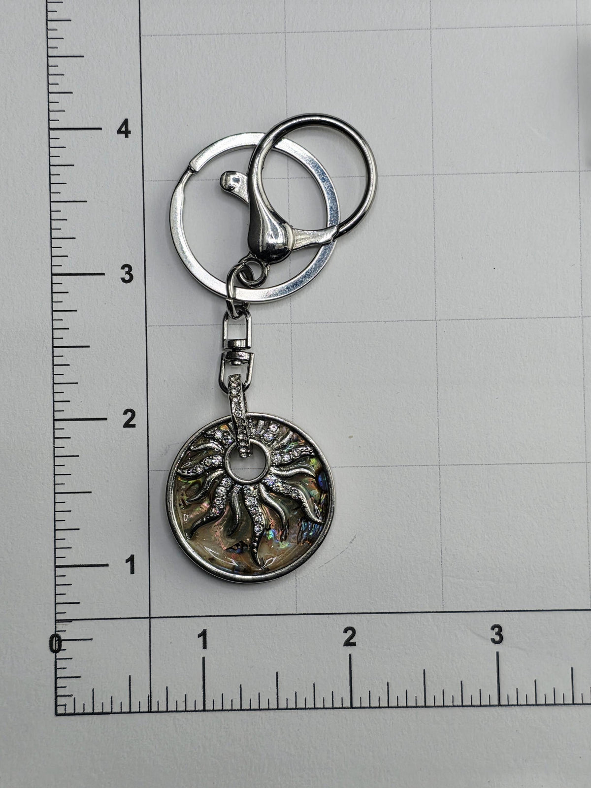 A keychain with a sun-shaped pendant and a metal ring attached to it, placed on a ruler for size comparison.