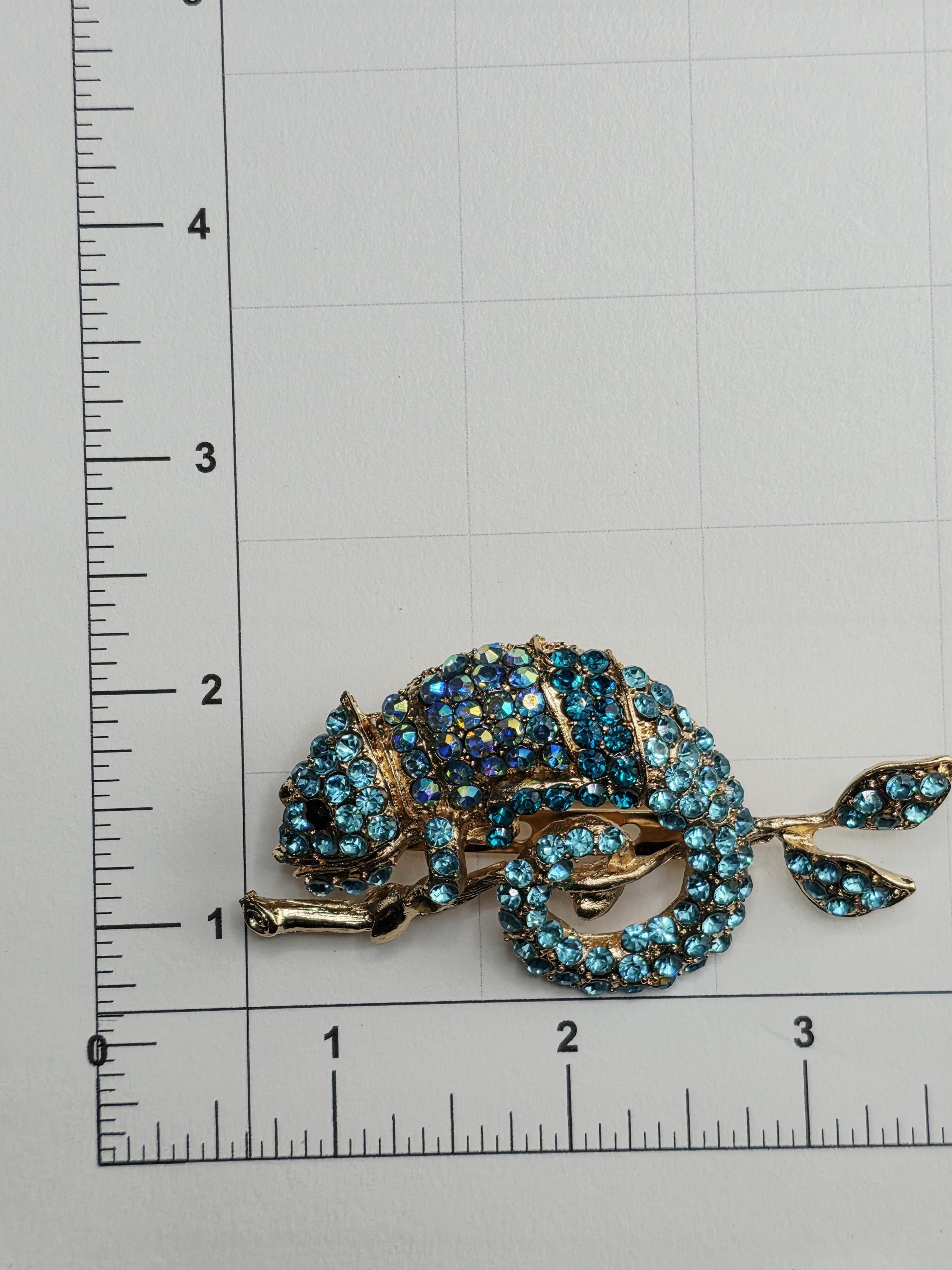 A decorative brooch with blue gemstones is placed on a ruler for size comparison.