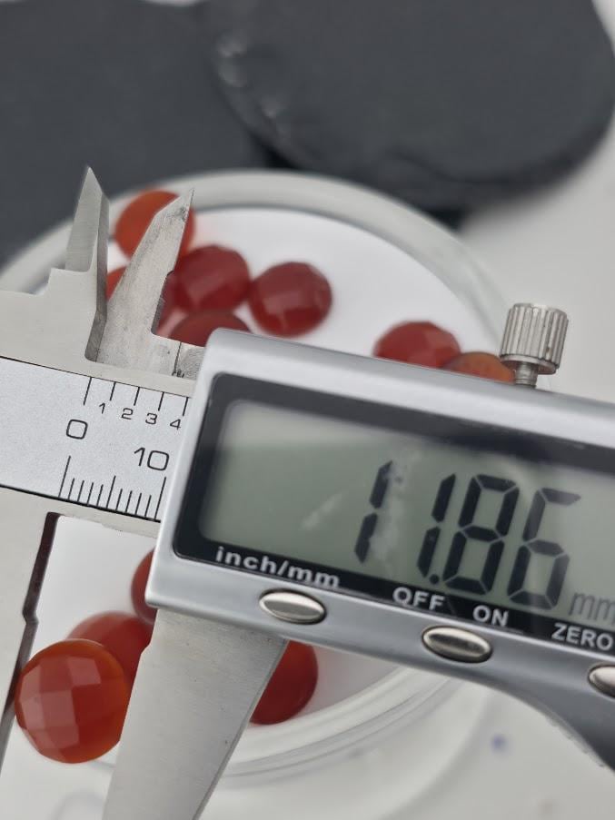 A digital caliper is being used to measure the size of a red object, which appears to be a small red ball or bead.