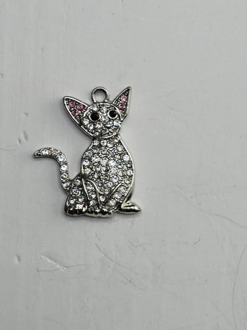 A silver-colored charm in the shape of a cat, adorned with small diamonds or crystals, is displayed against a plain white background.