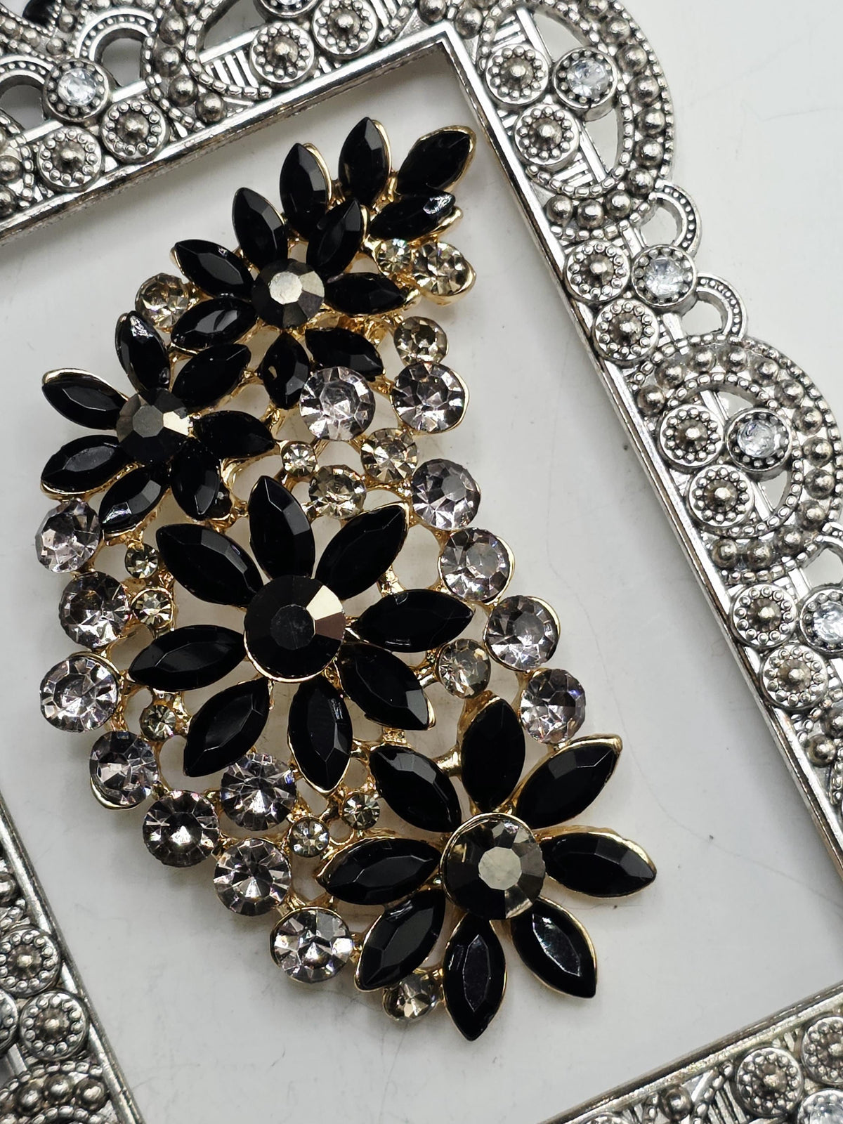 a close-up view of a decorative piece with a floral design, including black and gold elements, and numerous small clear gemstones.