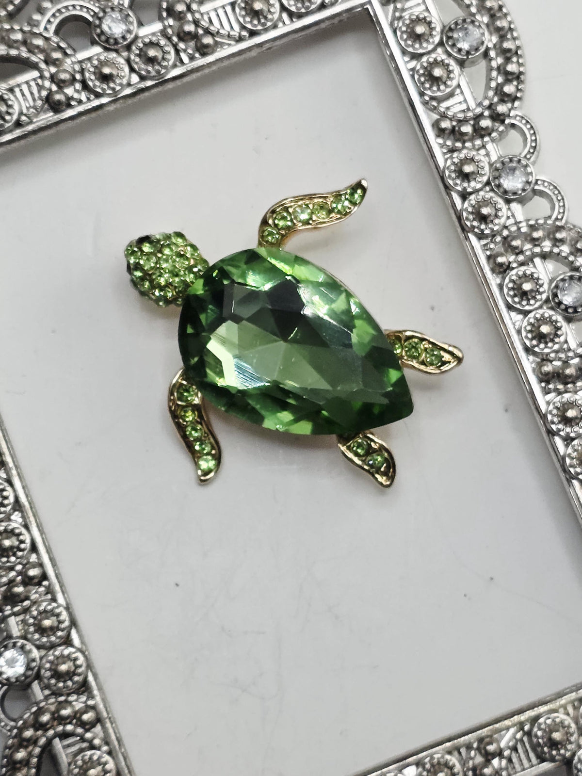 A decorative frame with a large green gemstone in the center, surrounded by smaller green gemstones.