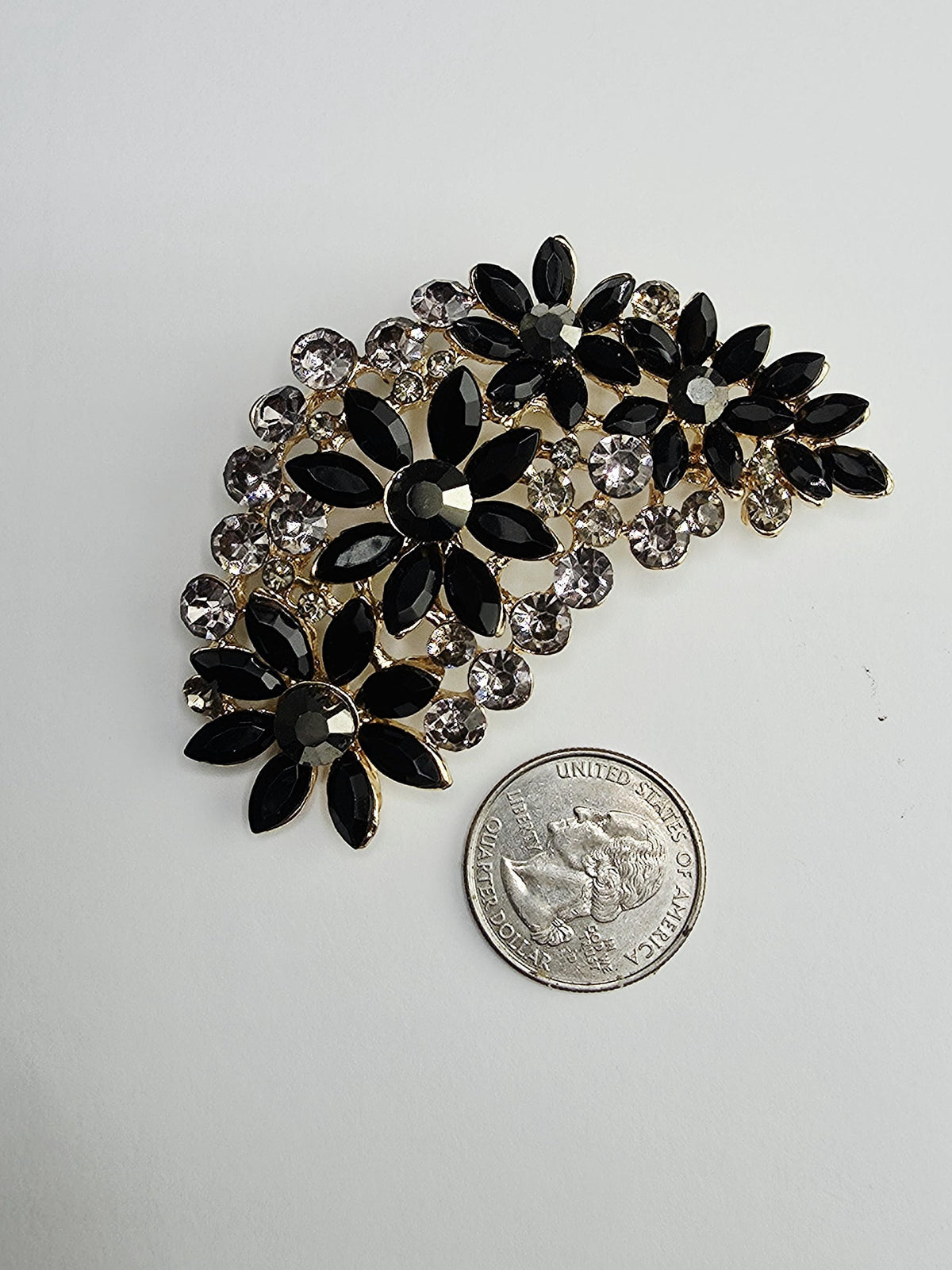 A decorative brooch with black and silver gemstones is placed next to a United States quarter coin.