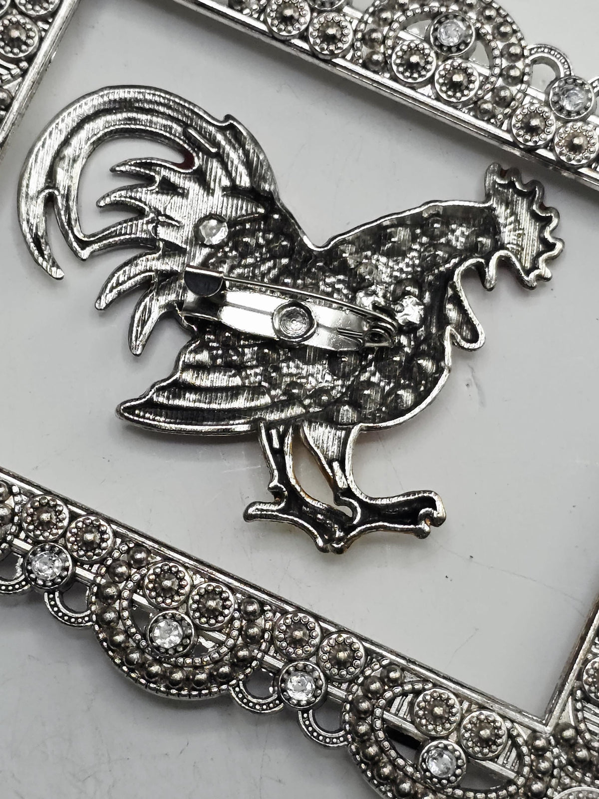 a decorative metal frame with a rooster design on it, which is placed on a white surface.