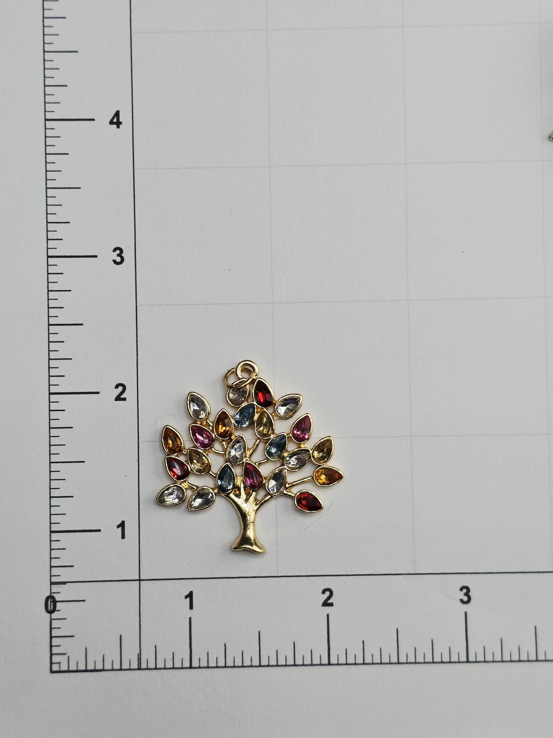 a decorative tree-shaped pendant made of colorful gemstones, placed on a ruler for size comparison.