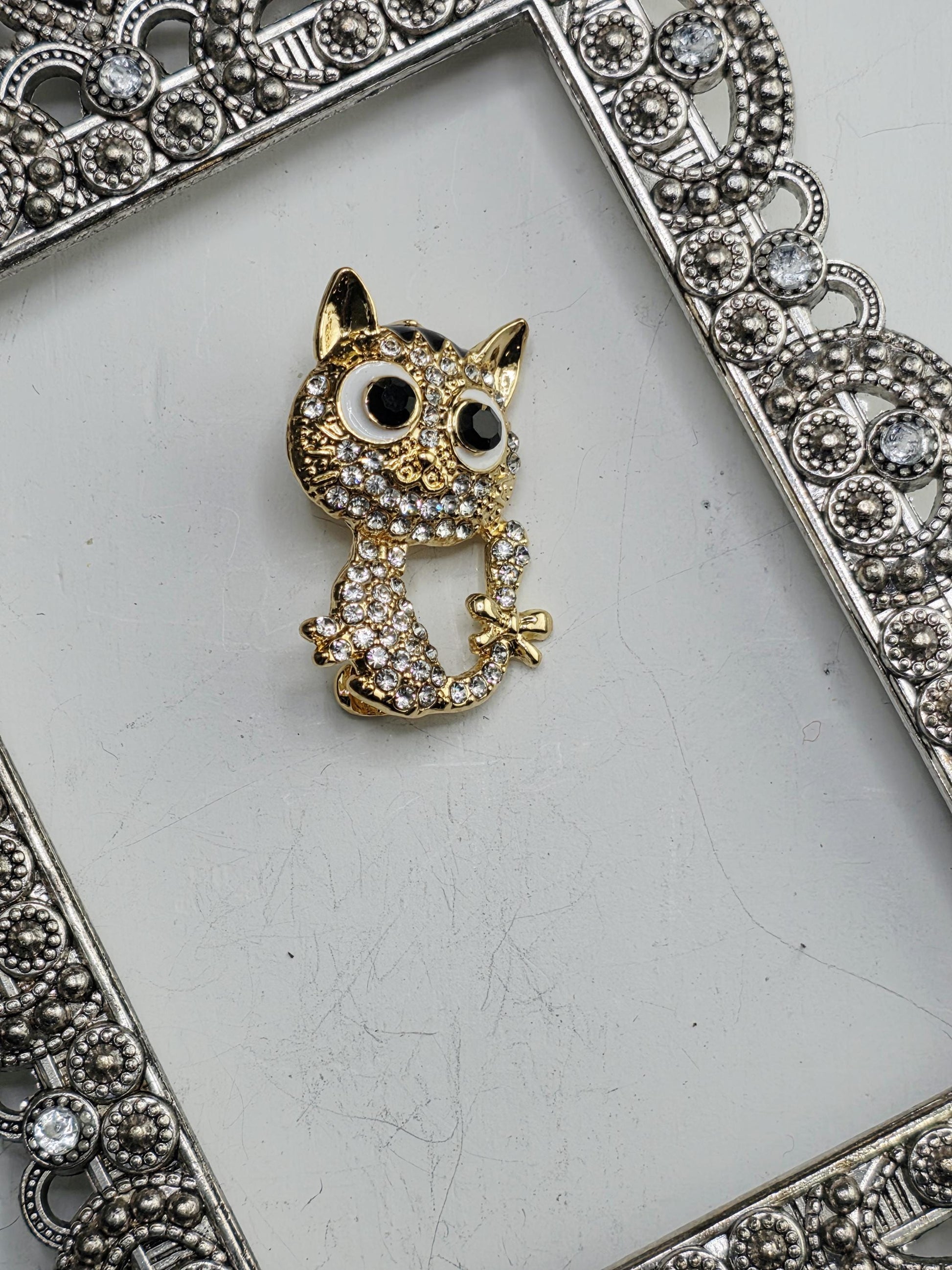 A decorative metal frame with a gold-colored owl-shaped charm or brooch on a white background.