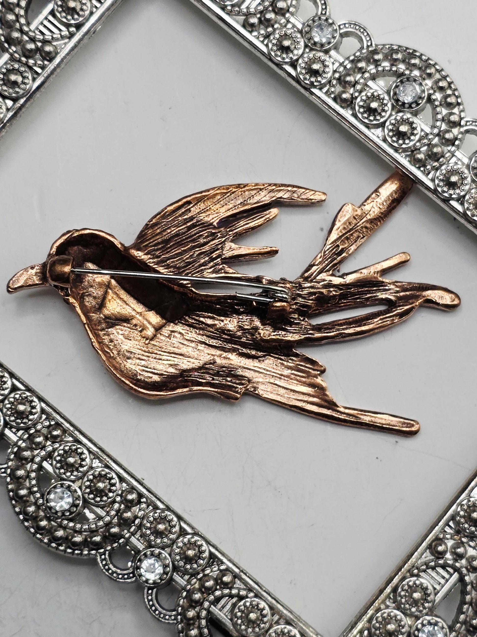 a close-up view of a decorative pin or brooch with a bird-like design, placed on a white surface.