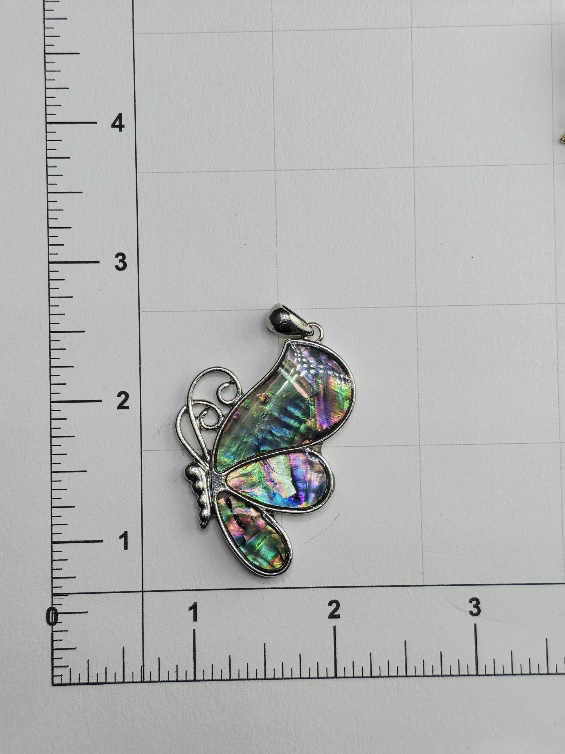 a colorful butterfly pendant with a multicolored iridescent pattern, resting on a ruler for scale.