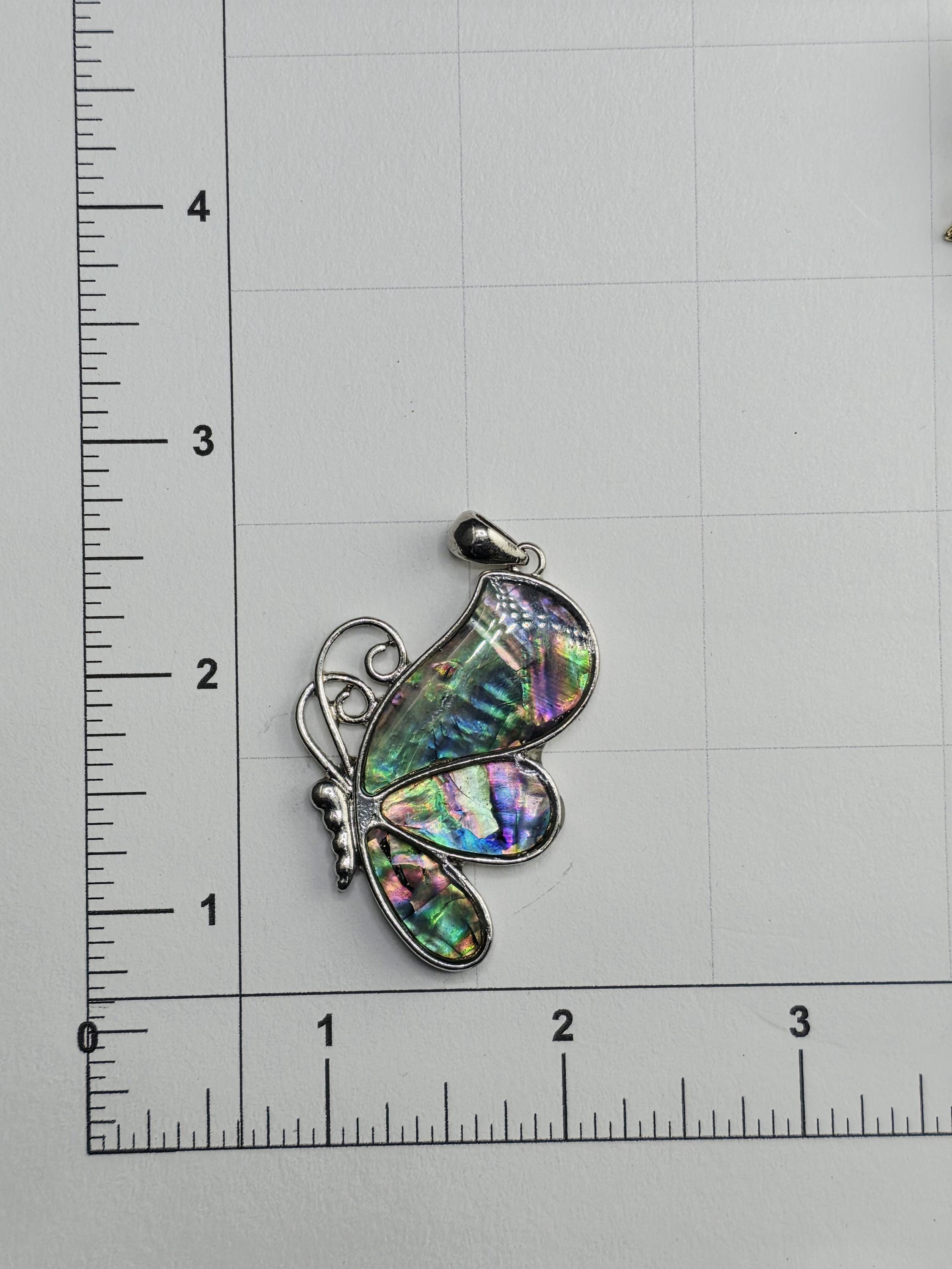 a colorful butterfly pendant with a multicolored iridescent pattern, resting on a ruler for scale.