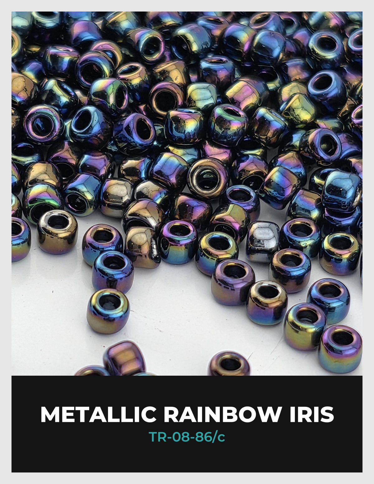 The image is a close-up of a pile of multicolored metal beads, including iridescent rainbow colors, scattered on a white surface.