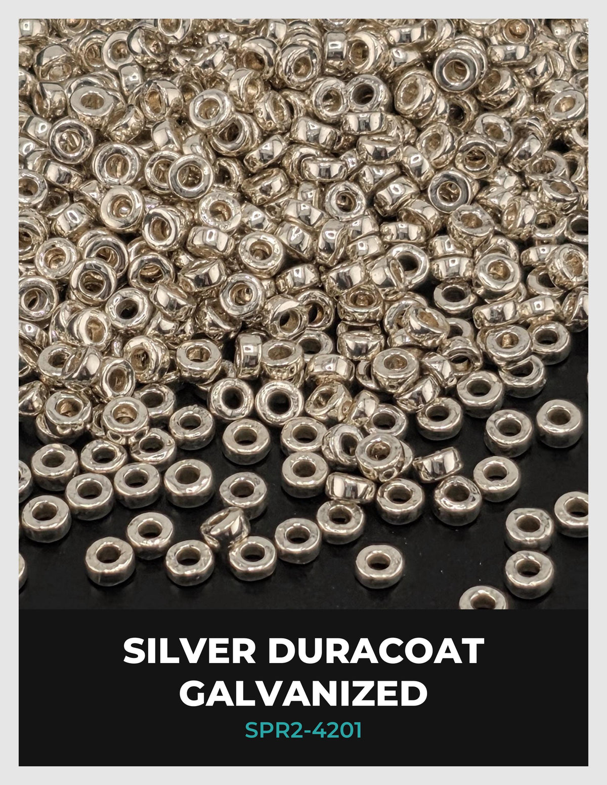 The image is a close-up of numerous silver-colored metal beads or coins scattered across a dark background.