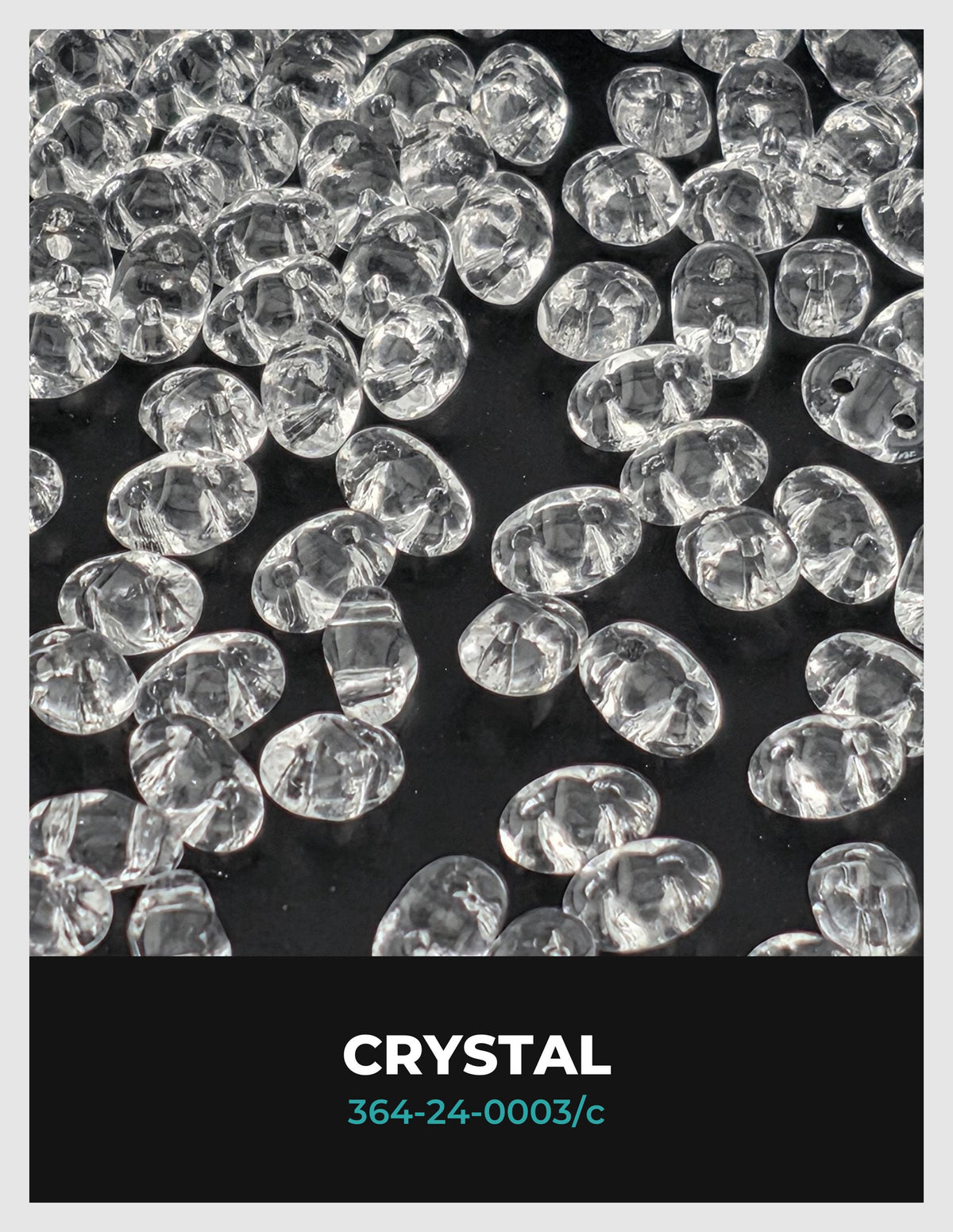 The image is a close-up of numerous clear crystal beads or stones, scattered across a dark background.